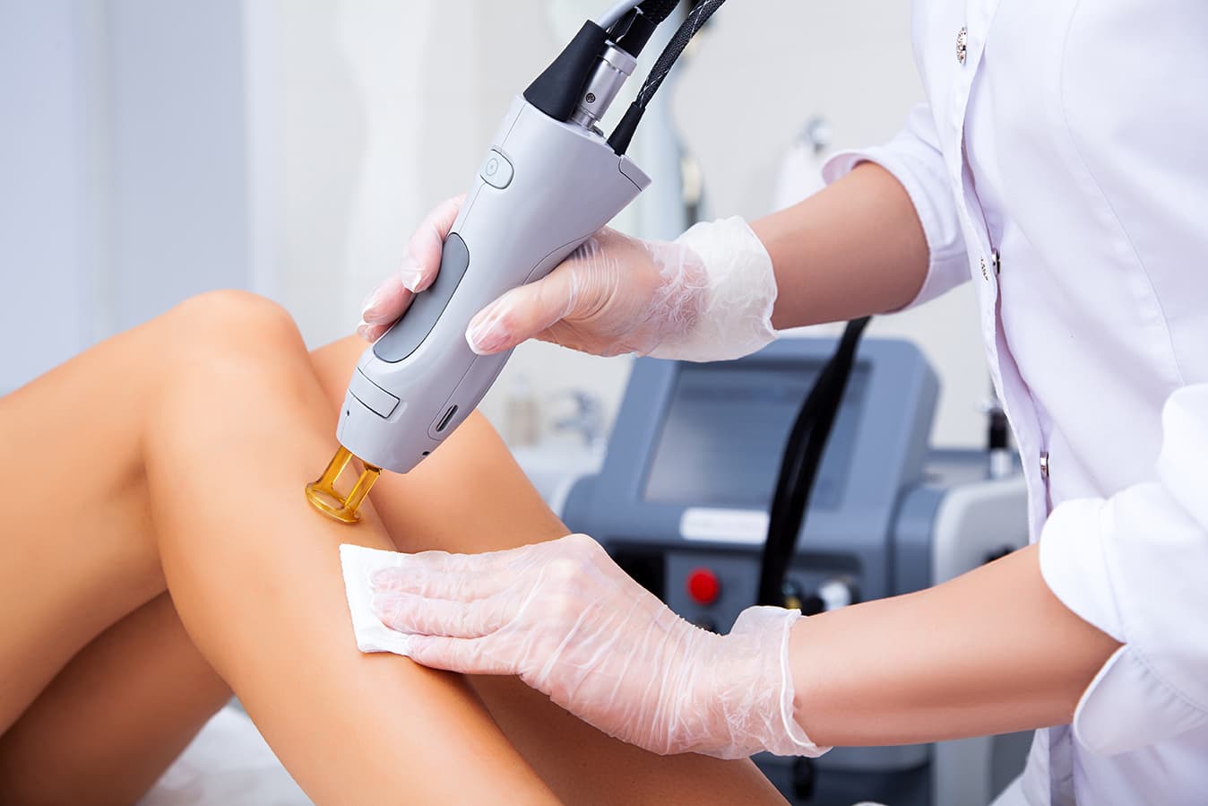 A specialist performing a laser procedure on a leg, an alexandrite laser used for hair and tattoo removal.